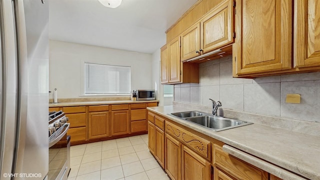 kitchen with backsplash, light countertops, light tile patterned flooring, stainless steel appliances, and a sink