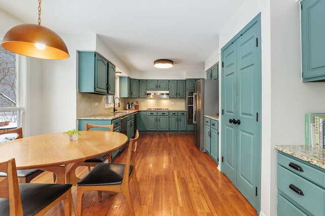 kitchen with under cabinet range hood, appliances with stainless steel finishes, green cabinets, decorative backsplash, and dark wood-style flooring