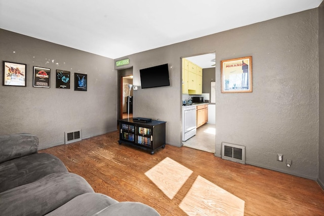 living area featuring visible vents, a textured wall, and light wood-style flooring