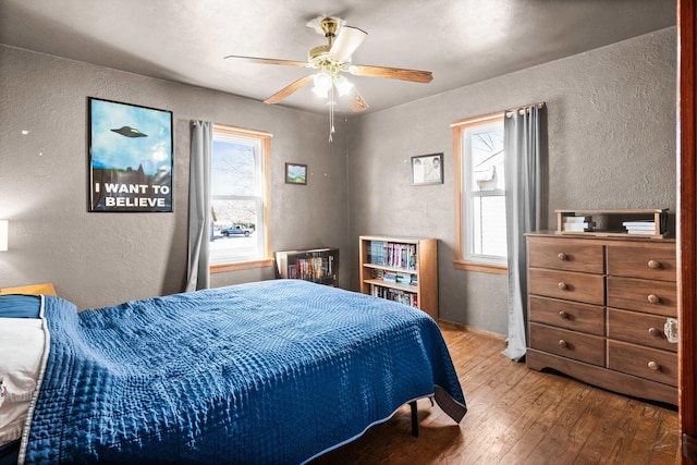 bedroom featuring multiple windows, a textured wall, and hardwood / wood-style floors