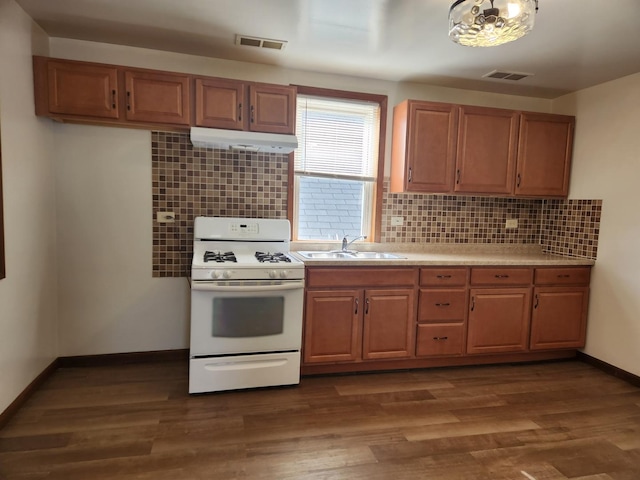 kitchen with white range with gas cooktop, visible vents, dark wood finished floors, under cabinet range hood, and a sink