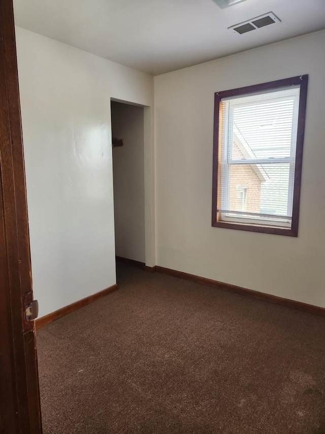 unfurnished room with visible vents, dark carpet, and baseboards