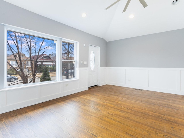 empty room with a ceiling fan, wainscoting, vaulted ceiling, and wood finished floors