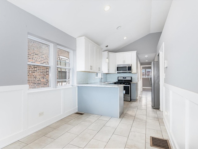 kitchen featuring stainless steel appliances, white cabinets, wainscoting, and a peninsula