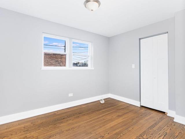 unfurnished bedroom with baseboards, dark wood finished floors, and a closet