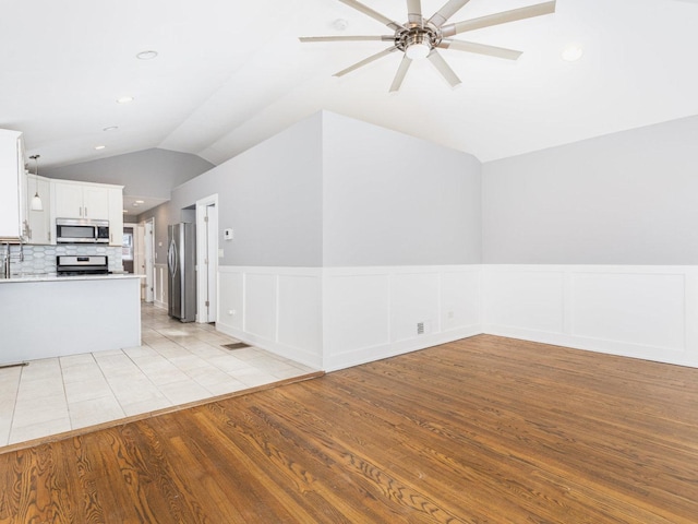 kitchen with open floor plan, appliances with stainless steel finishes, vaulted ceiling, and light wood-type flooring