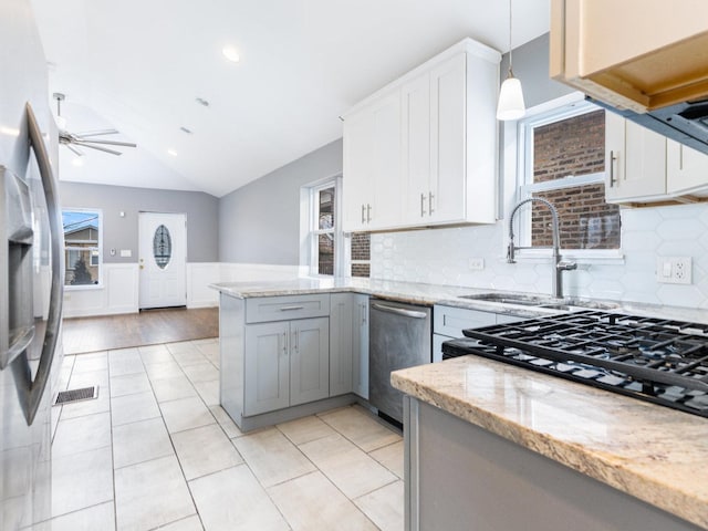 kitchen featuring light stone counters, a peninsula, a sink, vaulted ceiling, and appliances with stainless steel finishes