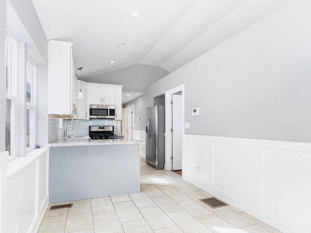 kitchen with visible vents, a wainscoted wall, appliances with stainless steel finishes, a peninsula, and vaulted ceiling