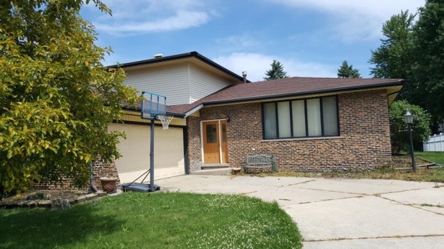 split level home with a garage, driveway, brick siding, and a front lawn