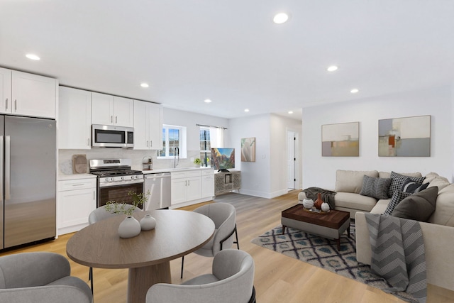 kitchen with open floor plan, stainless steel appliances, light wood-type flooring, and white cabinets