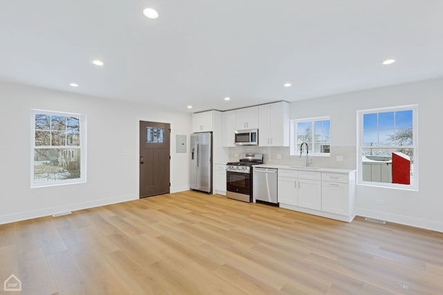 kitchen featuring tasteful backsplash, light wood-style flooring, appliances with stainless steel finishes, light countertops, and white cabinetry