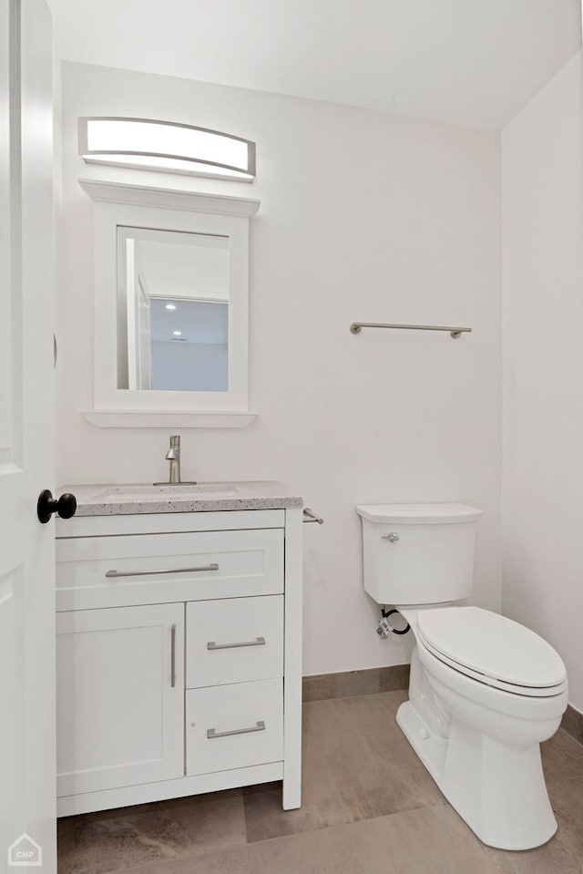 half bathroom featuring toilet, tile patterned flooring, baseboards, and vanity