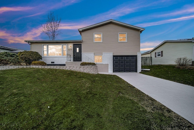 split level home with concrete driveway, an attached garage, and a front lawn