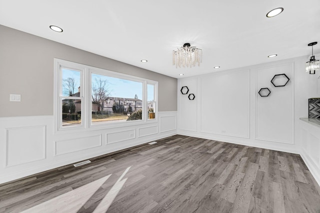 unfurnished dining area with a chandelier, wood finished floors, and a decorative wall