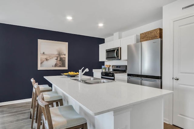 kitchen with stainless steel appliances, a kitchen island with sink, white cabinets, a sink, and a kitchen breakfast bar