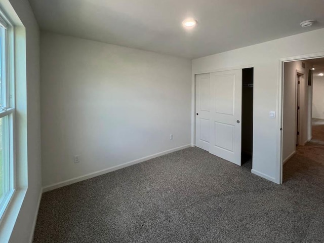 unfurnished bedroom featuring dark colored carpet, a closet, and baseboards
