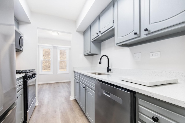 kitchen with light wood finished floors, baseboards, gray cabinets, stainless steel appliances, and a sink