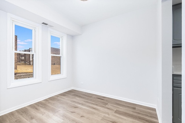 spare room featuring light wood-style floors, visible vents, and baseboards