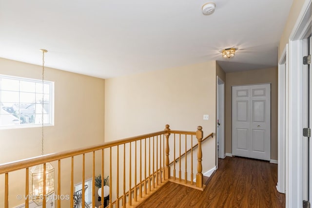 corridor featuring dark wood-type flooring, baseboards, a notable chandelier, and an upstairs landing