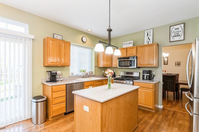 kitchen with light countertops, hanging light fixtures, light wood-style flooring, appliances with stainless steel finishes, and a sink