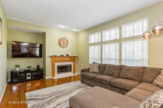 living room with a tile fireplace, baseboards, and wood finished floors