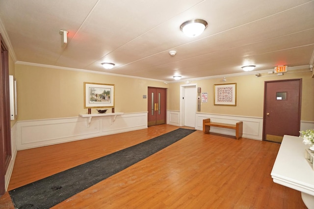 interior space with ornamental molding, a wainscoted wall, and wood finished floors