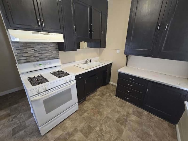 kitchen featuring white range with gas stovetop, a sink, dark cabinetry, under cabinet range hood, and backsplash