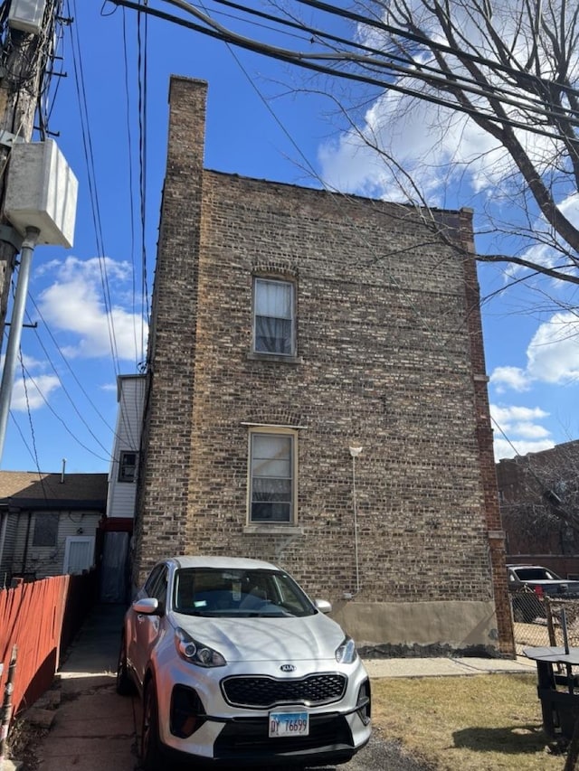 view of side of home featuring a chimney, fence, and brick siding