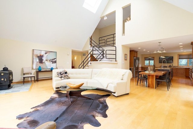 living room featuring high vaulted ceiling, stairway, light wood-type flooring, and a skylight