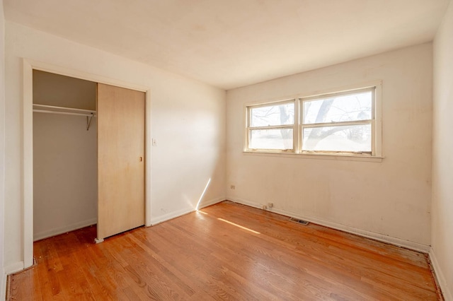 unfurnished bedroom featuring light wood-type flooring, baseboards, visible vents, and a closet