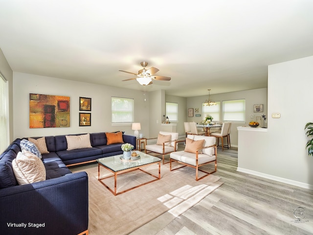 living area with light wood-type flooring, baseboards, and ceiling fan with notable chandelier