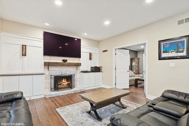 living room featuring wood finished floors, a fireplace, baseboards, visible vents, and recessed lighting