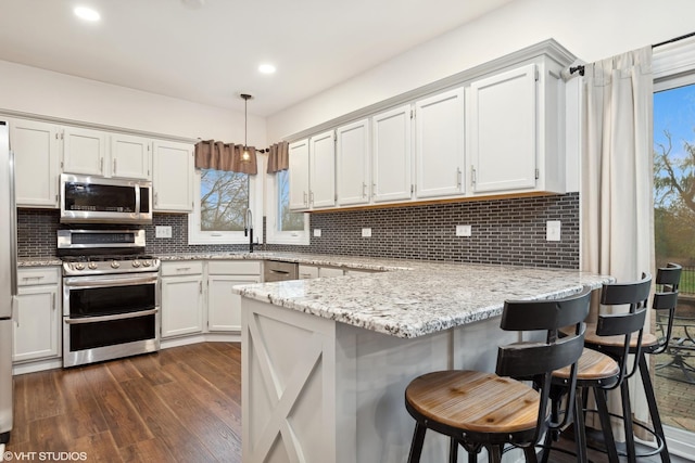 kitchen with stainless steel appliances, a peninsula, backsplash, and dark wood finished floors