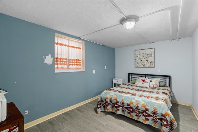 bedroom with wood finish floors, a textured ceiling, and baseboards