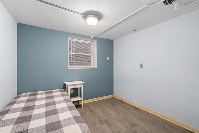 unfurnished bedroom featuring a textured ceiling, baseboards, and wood finished floors