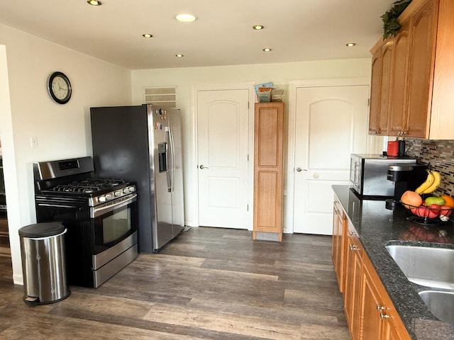 kitchen featuring backsplash, dark stone counters, stainless steel appliances, and dark wood-style flooring