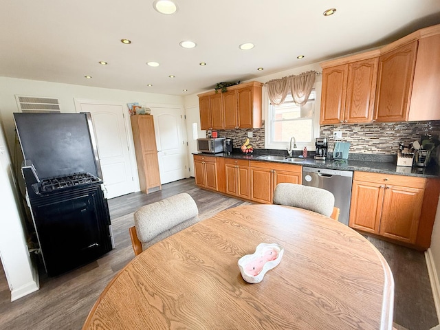 kitchen featuring tasteful backsplash, dark countertops, appliances with stainless steel finishes, a sink, and wood finished floors