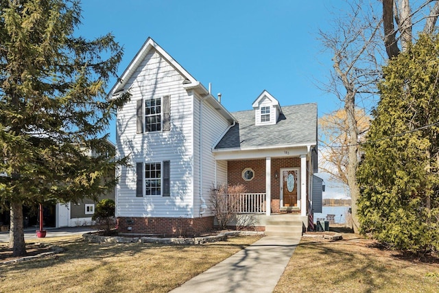 traditional home featuring covered porch, a shingled roof, and a front yard