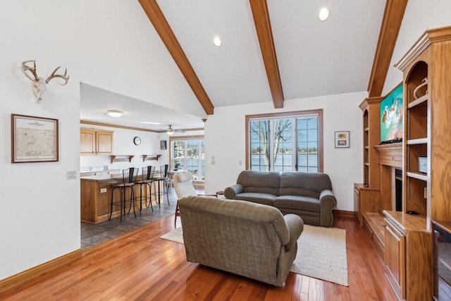 living area featuring vaulted ceiling with beams, a large fireplace, baseboards, a ceiling fan, and wood-type flooring