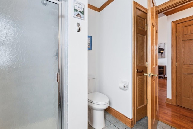 bathroom with toilet, crown molding, a shower stall, baseboards, and tile patterned flooring