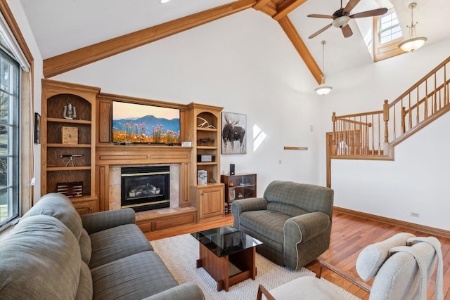 living area featuring stairway, wood finished floors, baseboards, ceiling fan, and a glass covered fireplace