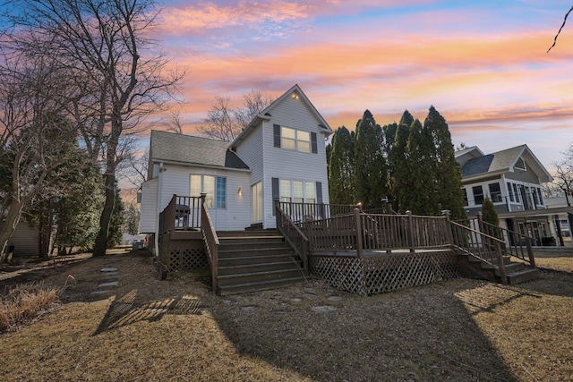 back of house at dusk with stairway, a wooden deck, and a shingled roof