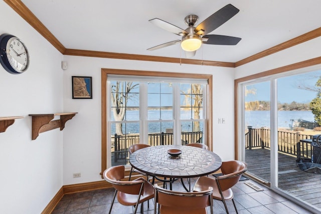 tiled dining room with a ceiling fan, a water view, a wealth of natural light, and ornamental molding