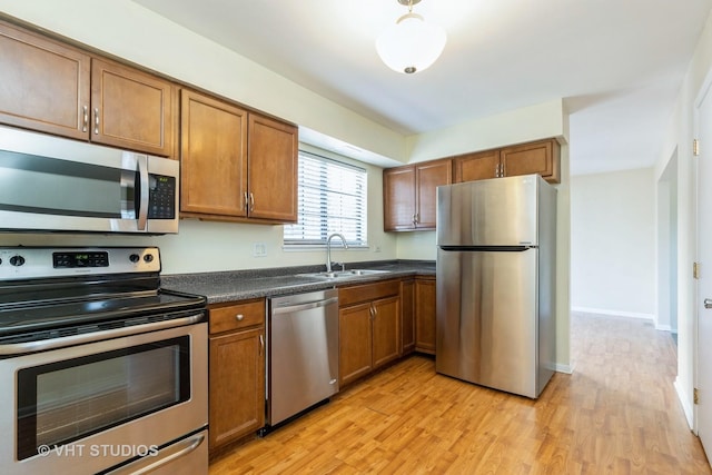 kitchen with dark countertops, light wood-style flooring, brown cabinets, stainless steel appliances, and a sink