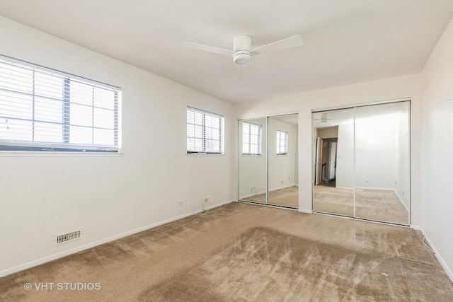 unfurnished bedroom with baseboards, visible vents, ceiling fan, carpet floors, and two closets