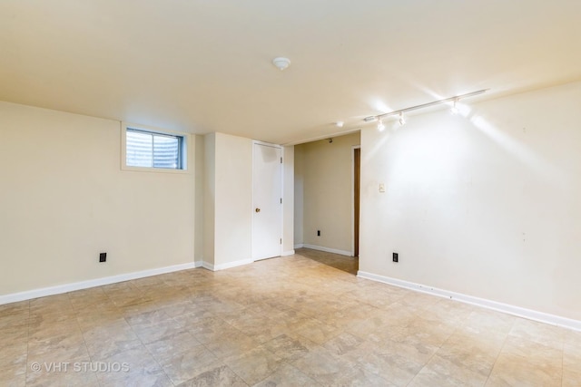 below grade area featuring rail lighting and baseboards