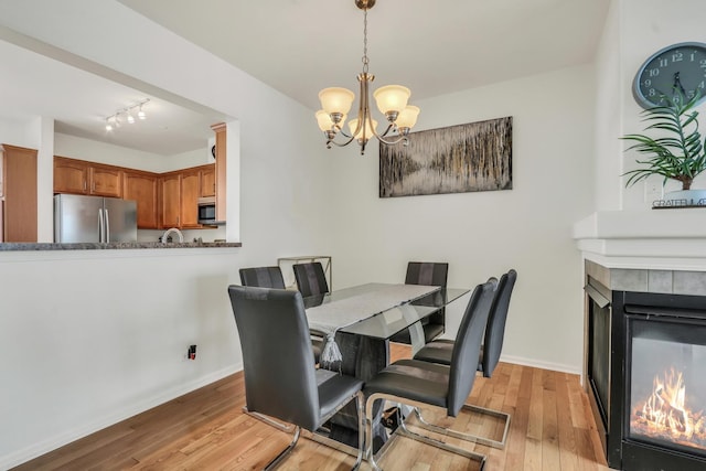 dining room featuring a tile fireplace, baseboards, light wood finished floors, and an inviting chandelier