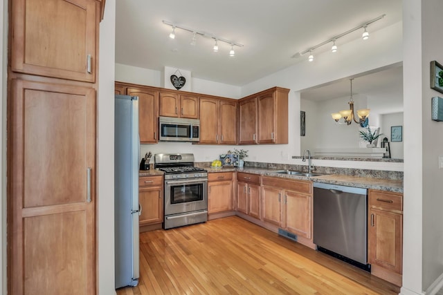 kitchen with pendant lighting, stainless steel appliances, light wood-style flooring, brown cabinetry, and a sink