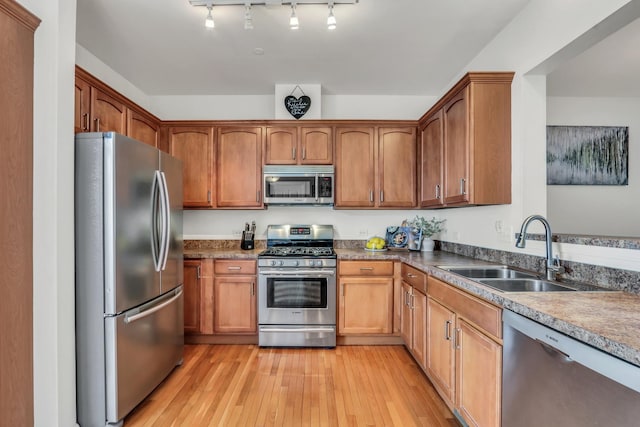 kitchen with appliances with stainless steel finishes, brown cabinets, a sink, and light wood finished floors