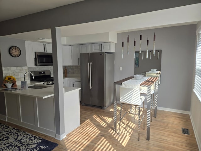 kitchen with light wood-style flooring, stainless steel appliances, a peninsula, light countertops, and tasteful backsplash